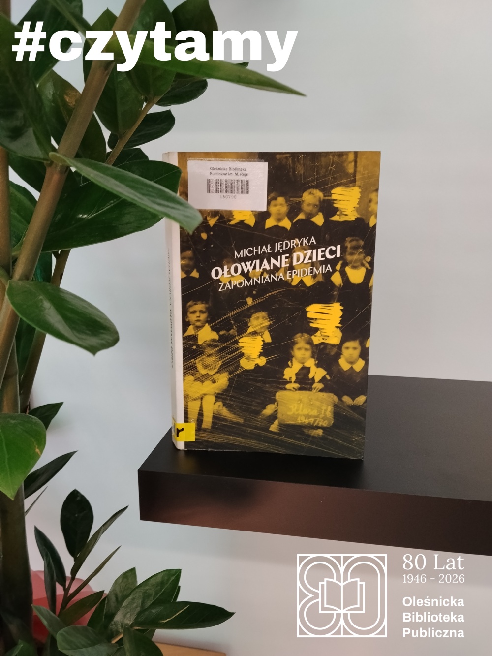 Okładka książki "Ołowiane dzieci" na tle białej ściany i rośliny