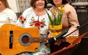 Dowie kobiety pozują do zdjęcia. Jedna trzyma gitarę, druga kwiatka doniczkowego