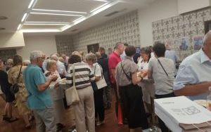 Kilkadziesiąt osób stoi w grupach, niektórzy trzymają talerze z jedzeniem