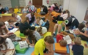 Uczniowie podstawówki siedzą na kolorowych matach i pufach, czytają książki