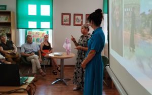 Dwie kobiety stoją przed grupą osób siedzących na krzesłach