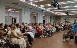Kilkadziesiąt osób siedzi na krzesłach na sali przed dwiema kobietami