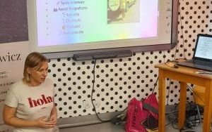 Kobieta siedzi na podłodze, przed nią leżą akcesoria podróżne, a na ścianie wyświetlana jest prezentacja