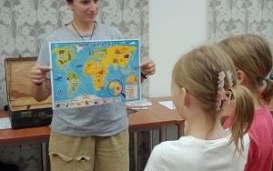 Dorosła osoba stoi przed grupą dzieci, trzymając mapę świata