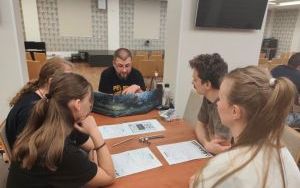Pięcioro dorosłych ludzi przy stoliku zapoznaje się z zasadami gry planszowej
