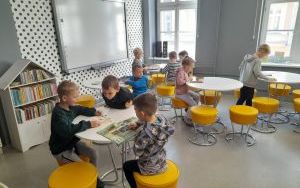 Dzieci siedzą przy okrągłych stolikach i czytają