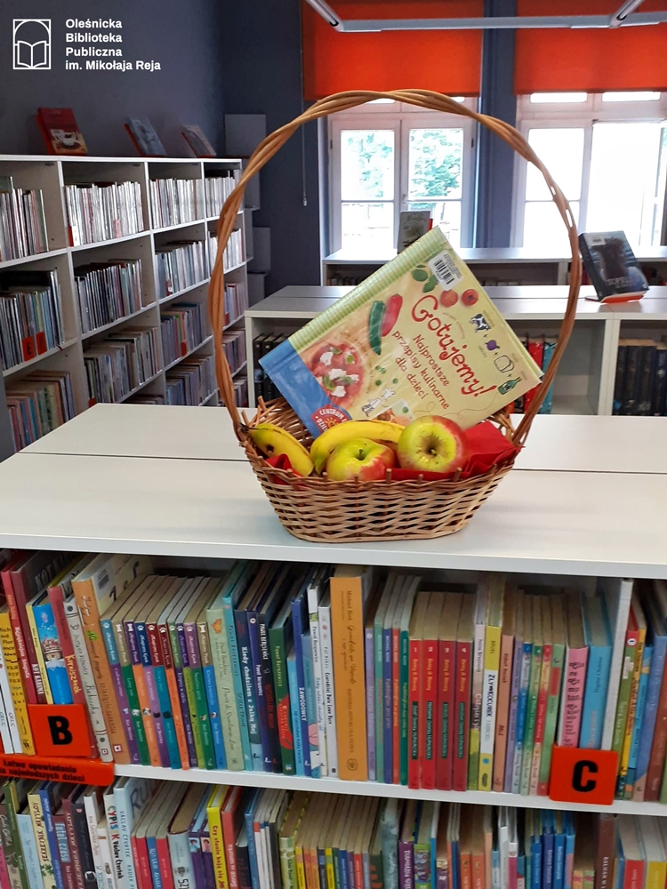 Książka kucharska w koszyczku z owocami ustawiona na regale bibliotecznym